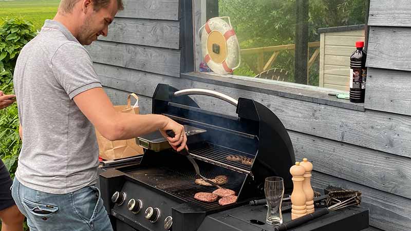 man staat te barbecueën in zijn tuin bij een gas bbq